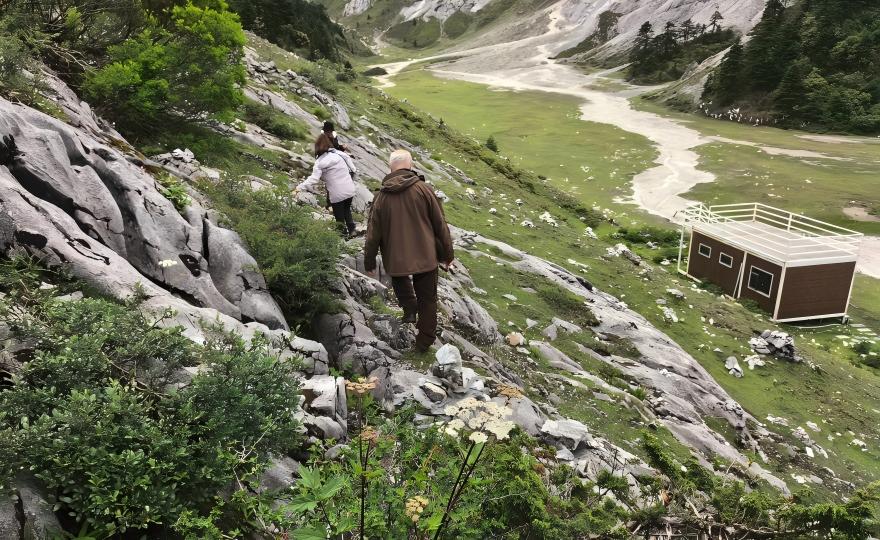 Two hikers descending scree slope with distant meadow, Yunnan butterfly tour terrain